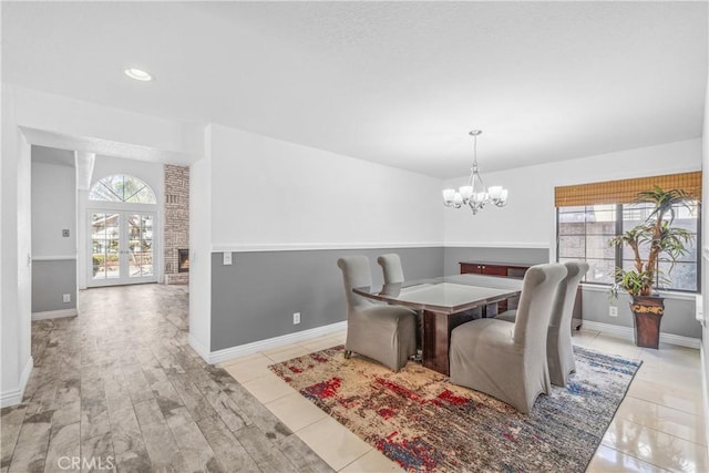 tiled dining area with a chandelier, a healthy amount of sunlight, a fireplace, and baseboards