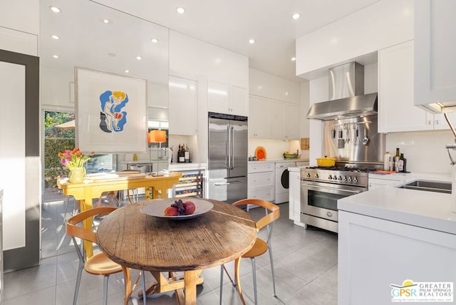 kitchen with high end appliances, independent washer and dryer, white cabinets, and wall chimney range hood