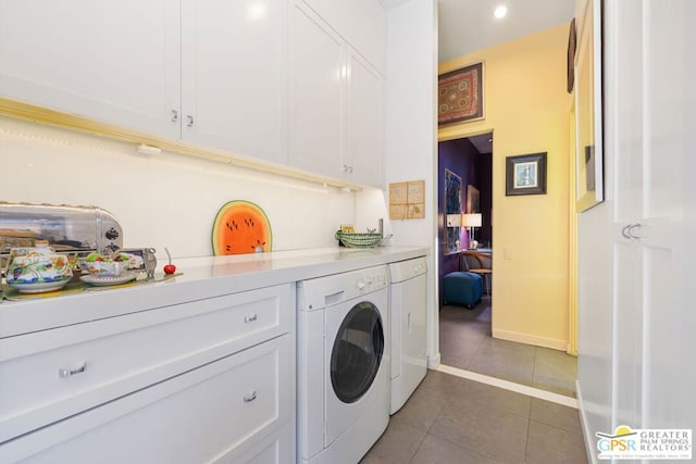 clothes washing area with dark tile patterned floors, washer and dryer, and cabinets