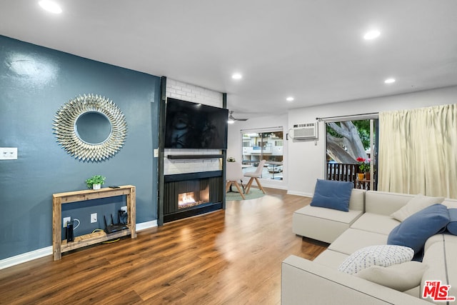 living room featuring a wall unit AC, ceiling fan, a fireplace, and wood-type flooring