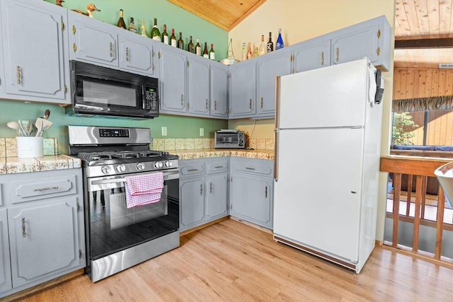 kitchen featuring lofted ceiling, stainless steel gas range oven, light wood-type flooring, white refrigerator, and wooden ceiling