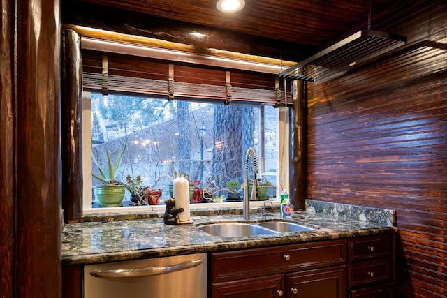 kitchen featuring wood walls, dark stone counters, stainless steel dishwasher, dark brown cabinetry, and sink