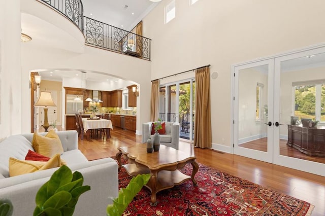 living room featuring a towering ceiling, french doors, ornamental molding, and wood-type flooring