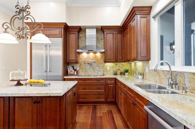 kitchen featuring wall chimney range hood, sink, pendant lighting, stainless steel appliances, and light stone counters