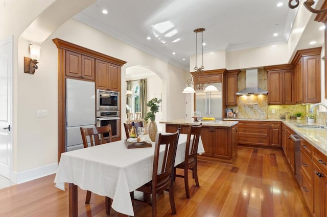 kitchen featuring pendant lighting, appliances with stainless steel finishes, tasteful backsplash, a center island, and wall chimney range hood