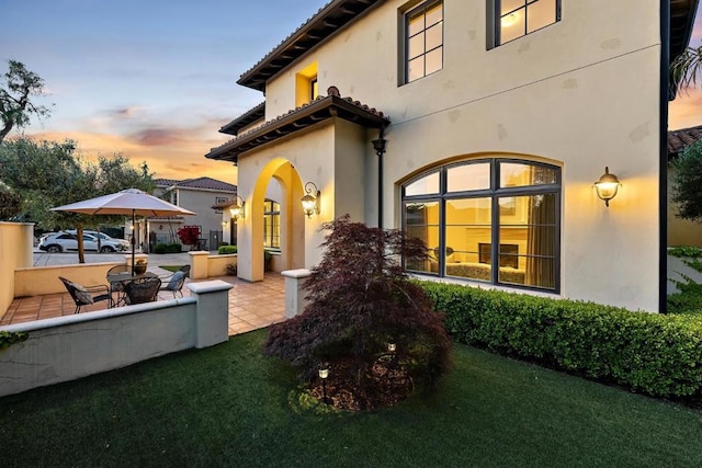 back house at dusk with a patio area and a lawn