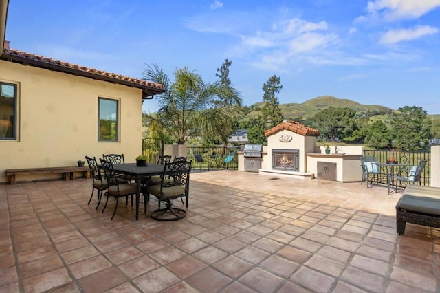 view of patio with exterior fireplace, a mountain view, and a grill