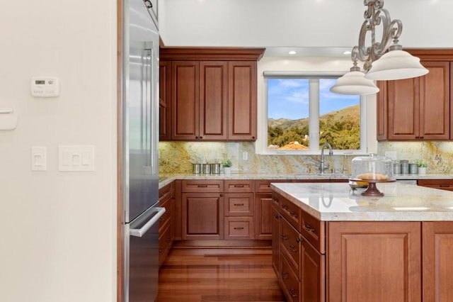 kitchen featuring high quality fridge, hanging light fixtures, sink, backsplash, and light stone counters