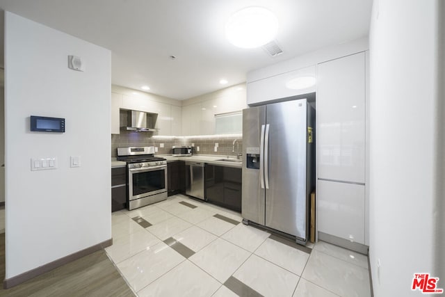 kitchen with tasteful backsplash, wall chimney range hood, sink, white cabinetry, and stainless steel appliances