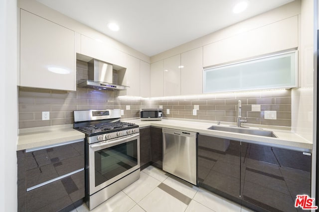 kitchen featuring white cabinetry, appliances with stainless steel finishes, light tile patterned flooring, wall chimney range hood, and sink