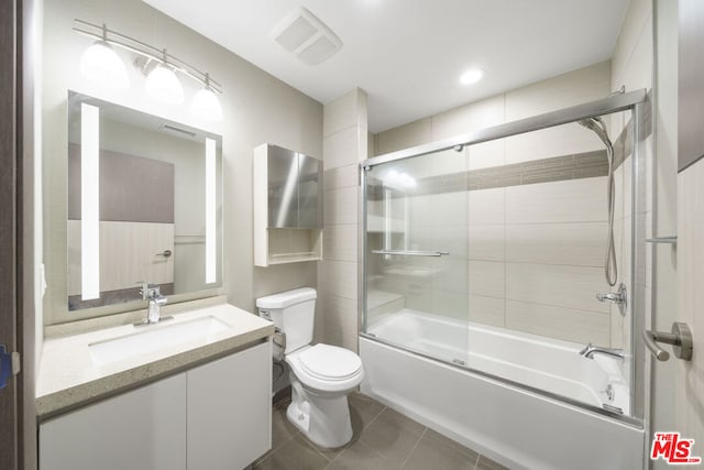 full bathroom with combined bath / shower with glass door, vanity, tile patterned flooring, and toilet