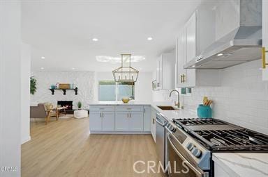 kitchen featuring appliances with stainless steel finishes, wall chimney exhaust hood, decorative light fixtures, white cabinetry, and sink