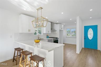 kitchen with white cabinetry, stainless steel range oven, wall chimney exhaust hood, and hanging light fixtures