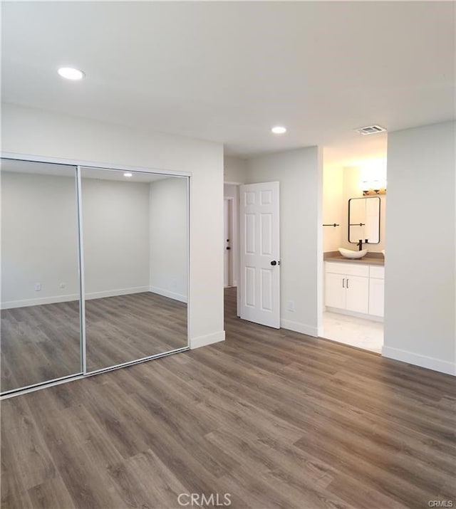 unfurnished bedroom featuring dark wood-type flooring, sink, ensuite bathroom, and a closet