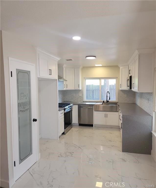 kitchen with appliances with stainless steel finishes, wall chimney exhaust hood, white cabinetry, sink, and backsplash