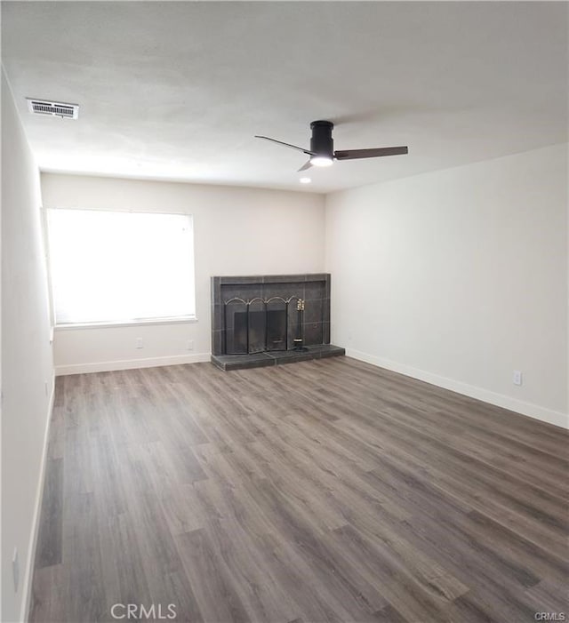 unfurnished living room featuring ceiling fan, wood-type flooring, and a tiled fireplace