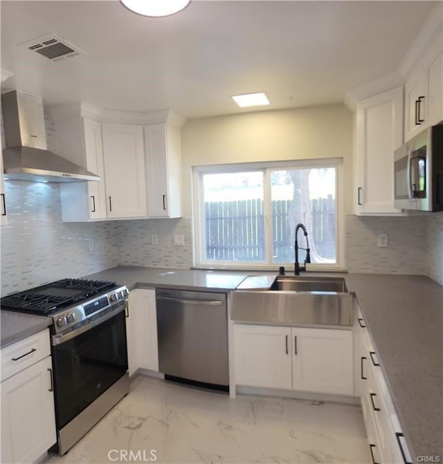 kitchen with stainless steel appliances, sink, white cabinetry, and wall chimney range hood