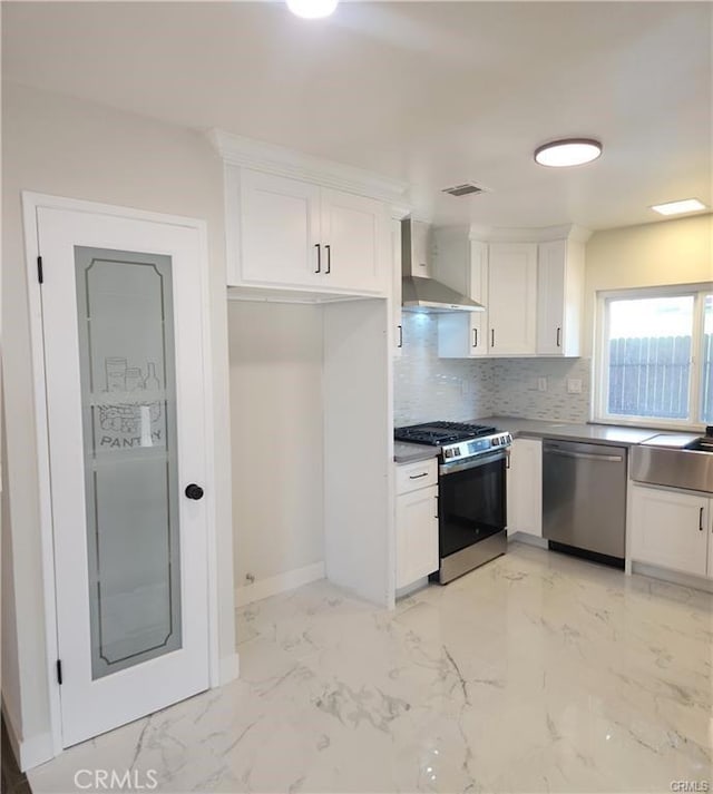 kitchen with appliances with stainless steel finishes, tasteful backsplash, wall chimney exhaust hood, white cabinets, and sink