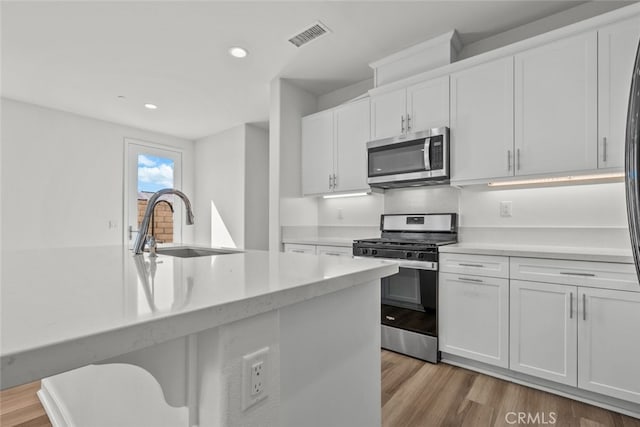 kitchen with white cabinets, appliances with stainless steel finishes, sink, and light wood-type flooring