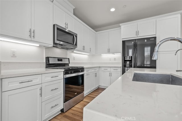 kitchen with light hardwood / wood-style floors, sink, appliances with stainless steel finishes, white cabinets, and light stone counters