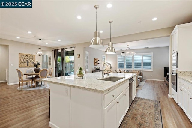 kitchen featuring white cabinetry, a kitchen island with sink, sink, and decorative light fixtures