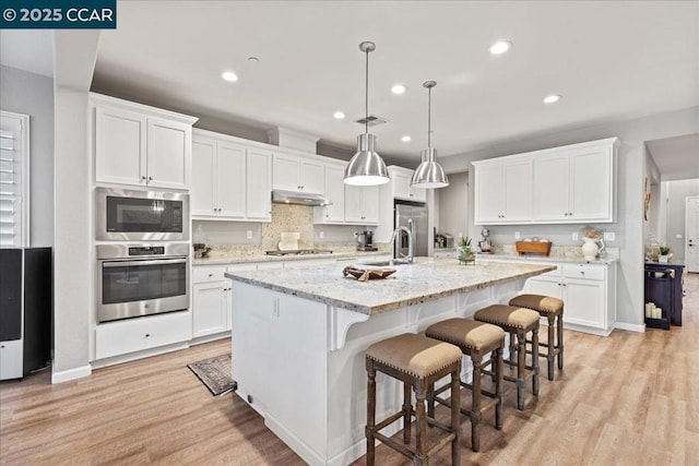 kitchen featuring pendant lighting, stainless steel appliances, an island with sink, and white cabinets