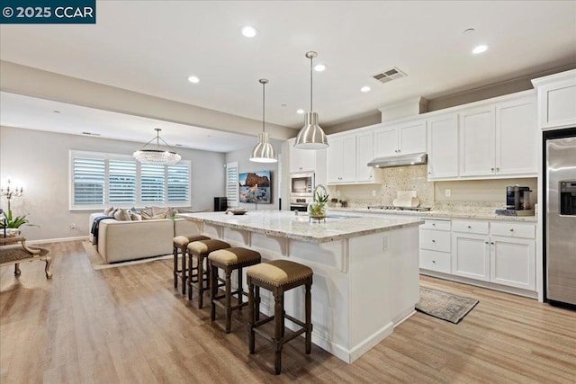 kitchen with pendant lighting, stainless steel appliances, a kitchen island with sink, and white cabinets