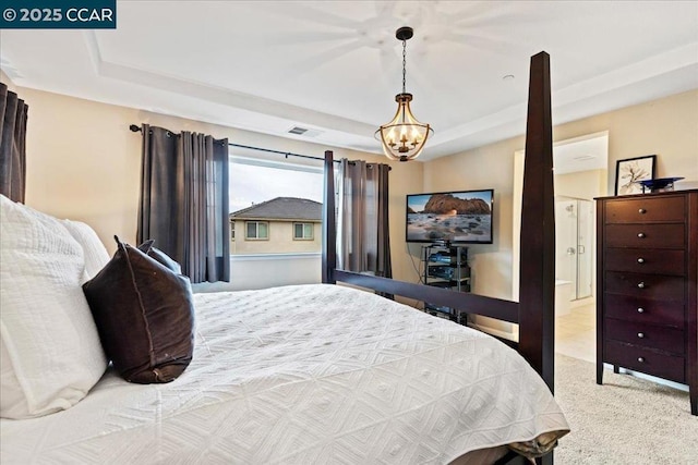 bedroom with ensuite bathroom, a raised ceiling, light carpet, and a notable chandelier