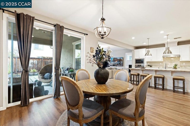 dining room with a notable chandelier, wood-type flooring, sink, and a wealth of natural light