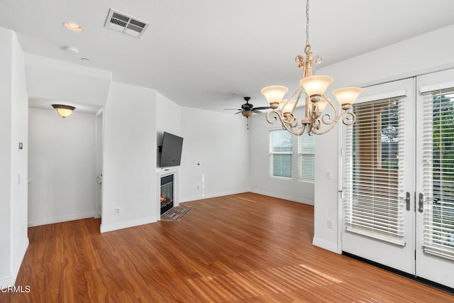 unfurnished living room with a wealth of natural light, ceiling fan with notable chandelier, and hardwood / wood-style flooring