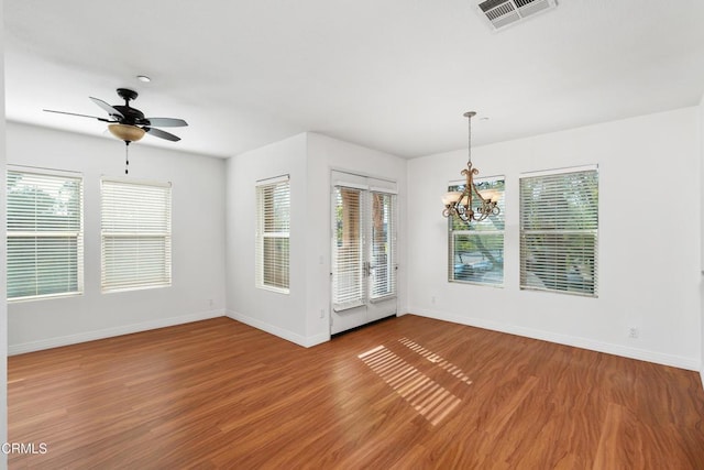 unfurnished room with ceiling fan with notable chandelier, hardwood / wood-style floors, and a wealth of natural light