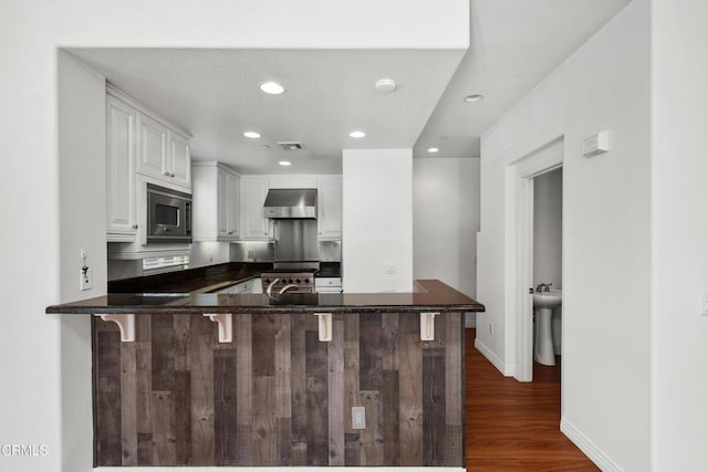 kitchen featuring range hood, white cabinets, kitchen peninsula, and a kitchen breakfast bar