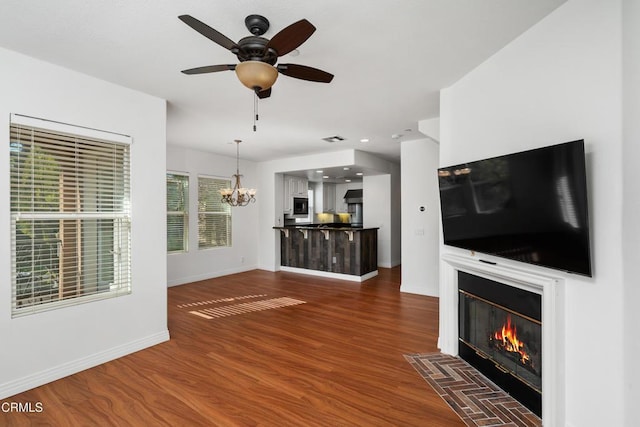 unfurnished living room with ceiling fan with notable chandelier and dark wood-type flooring