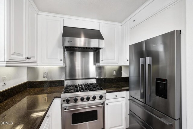 kitchen with white cabinetry, appliances with stainless steel finishes, ventilation hood, and dark stone counters