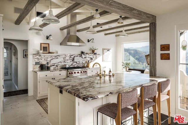 kitchen with backsplash, beamed ceiling, white cabinetry, high end stainless steel range oven, and wall chimney exhaust hood