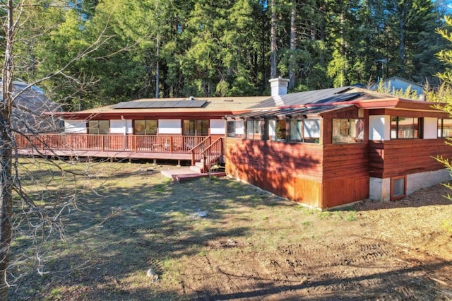 back of property with a deck, a lawn, and solar panels