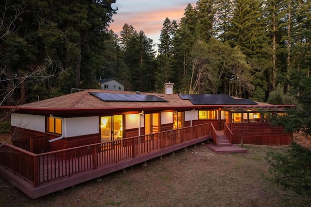 back house at dusk with a deck and solar panels