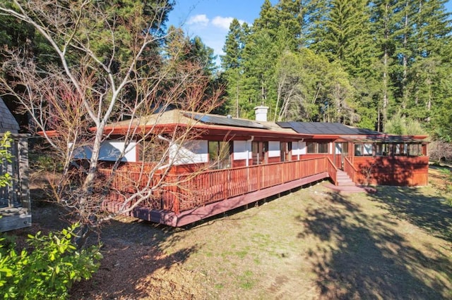 rear view of property with a deck, a lawn, and solar panels