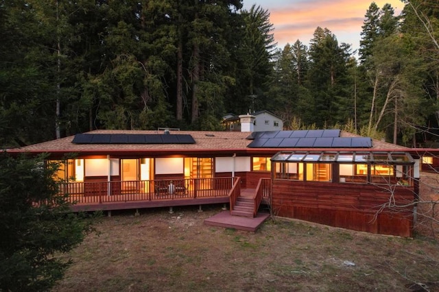 back house at dusk with a deck and solar panels