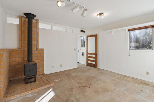 unfurnished living room featuring track lighting, concrete floors, and a wood stove