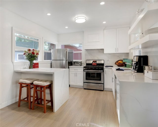 kitchen with light hardwood / wood-style floors, white cabinetry, light stone countertops, appliances with stainless steel finishes, and a breakfast bar area