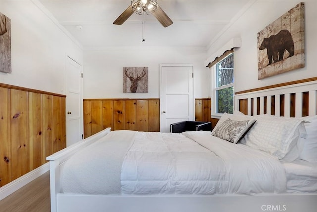 bedroom with ceiling fan, ornamental molding, wood-type flooring, and wood walls