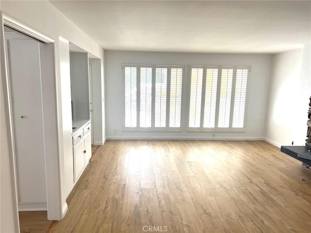 unfurnished living room featuring baseboards and light wood finished floors