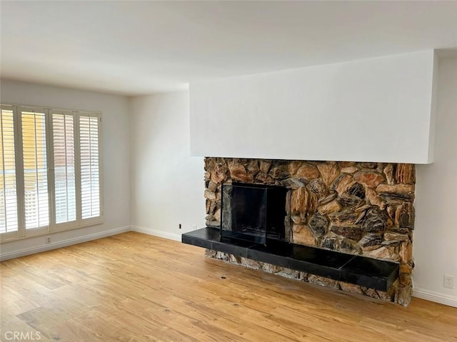 living room with a stone fireplace, baseboards, and wood finished floors