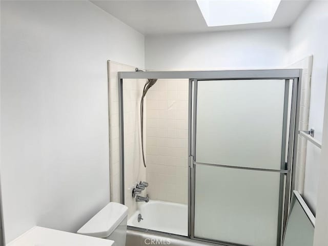 bathroom featuring a skylight, toilet, and combined bath / shower with glass door