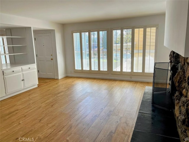 unfurnished living room with plenty of natural light, light wood-type flooring, and baseboards