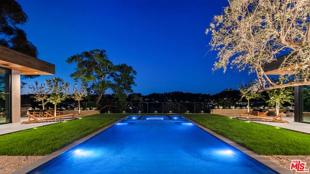 pool at night featuring a patio area and a yard