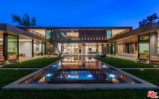 back house at night featuring a swimming pool with hot tub, a yard, an outdoor hangout area, and a patio