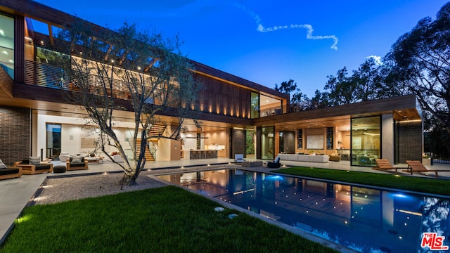 pool at dusk featuring a patio area, outdoor lounge area, and a yard