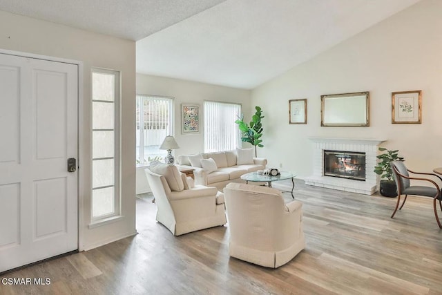 living room with light wood-type flooring, a textured ceiling, a fireplace, and lofted ceiling